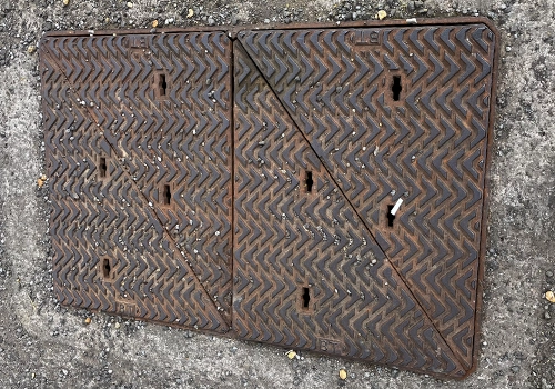 Rectangular metal telecoms cover, split into two squares, with a raised chevron pattern. 