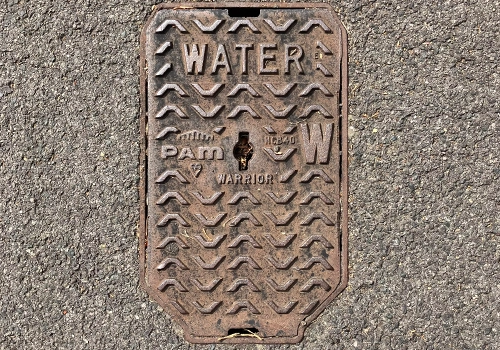 A rectangular water washout cover within the road. The cover has a raised chevron patter with raised text stating water at the top. 