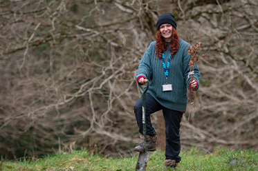 Volunteer for the mudpie explorer group planting a tree in a field smiling